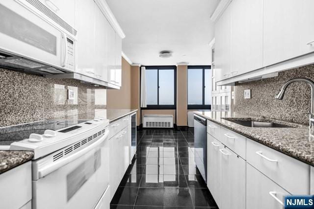 kitchen with tasteful backsplash, white cabinetry, a sink, dark tile patterned flooring, and white appliances