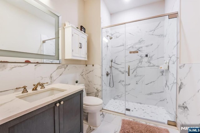 bathroom featuring toilet, marble finish floor, a marble finish shower, tile walls, and vanity