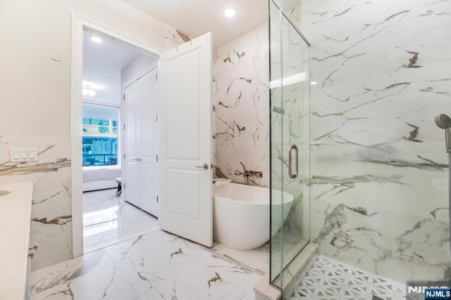 ensuite bathroom featuring marble finish floor, ensuite bath, a marble finish shower, a soaking tub, and stone wall