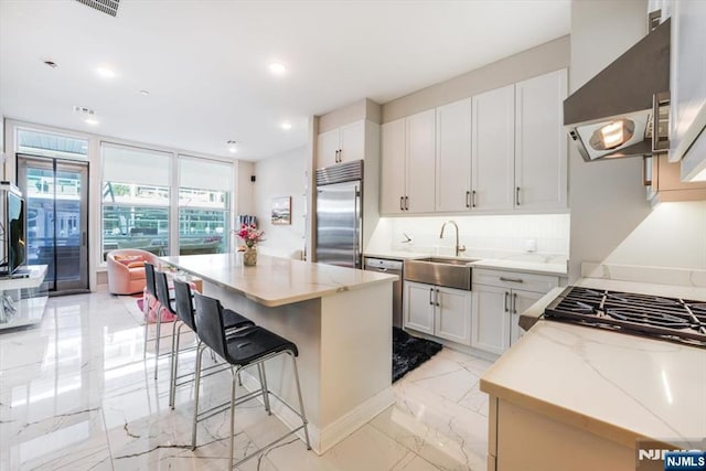 kitchen featuring stainless steel built in fridge, marble finish floor, a sink, backsplash, and ventilation hood