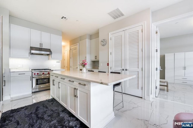 kitchen featuring under cabinet range hood, visible vents, marble finish floor, and designer stove