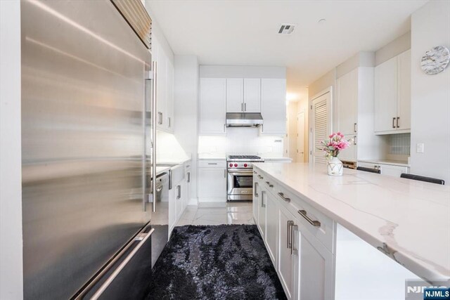 kitchen with under cabinet range hood, visible vents, white cabinets, and high quality appliances