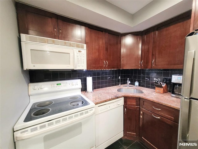 kitchen with white appliances, tasteful backsplash, light stone countertops, dark tile patterned floors, and a sink