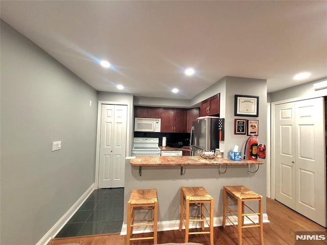 kitchen featuring recessed lighting, a kitchen breakfast bar, white appliances, a peninsula, and baseboards