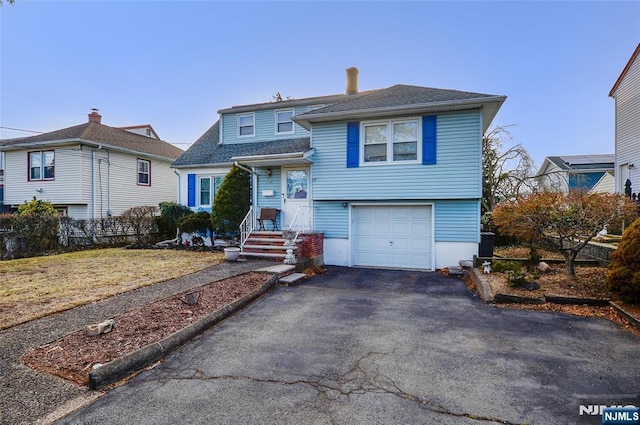 tri-level home with a garage, driveway, fence, and a shingled roof