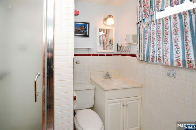 bathroom with a stall shower, wainscoting, toilet, vanity, and tile walls