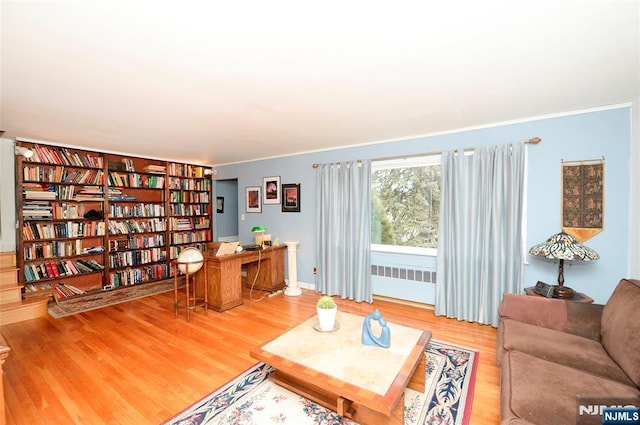 living area with radiator, ornamental molding, and wood finished floors