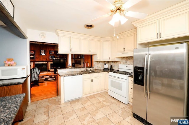 kitchen featuring a sink, a peninsula, dark stone counters, white appliances, and under cabinet range hood