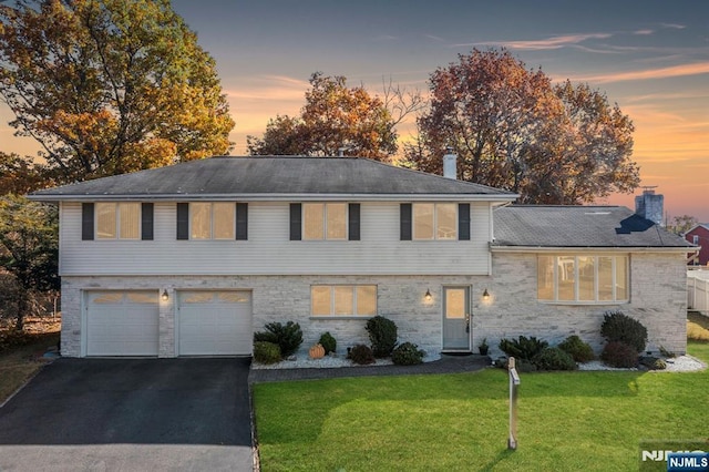 split level home featuring aphalt driveway, a yard, a chimney, and a garage