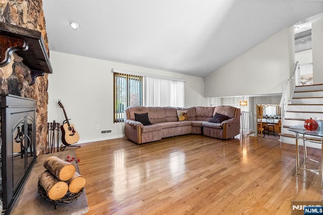 living area featuring baseboards, visible vents, stairway, wood finished floors, and a stone fireplace