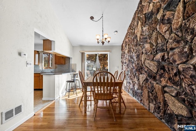 dining room featuring a notable chandelier, light wood finished floors, visible vents, a textured wall, and vaulted ceiling