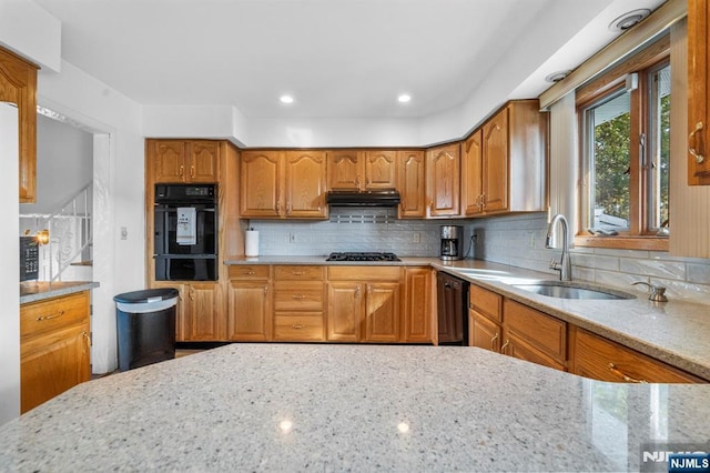 kitchen featuring light stone counters, backsplash, a sink, under cabinet range hood, and black appliances