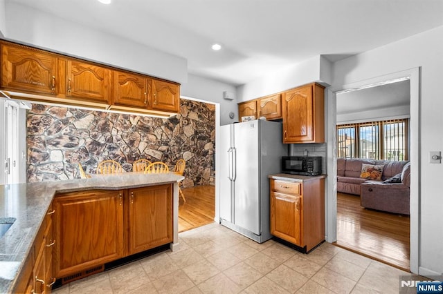 kitchen featuring freestanding refrigerator, black microwave, brown cabinets, and recessed lighting