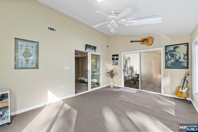 carpeted empty room with a skylight, ceiling fan, visible vents, and baseboards