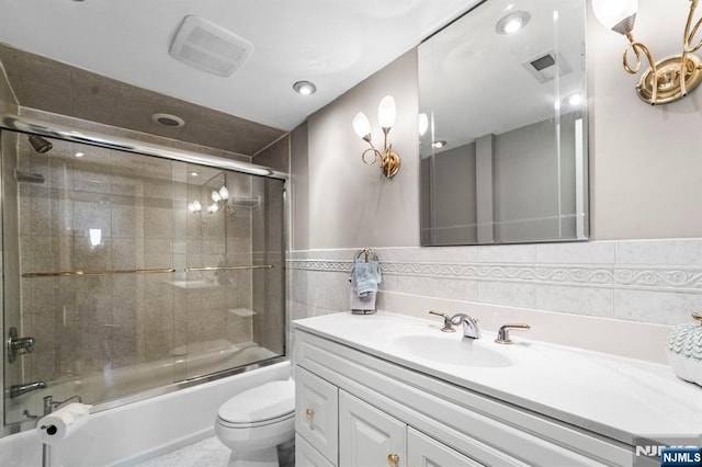 bathroom featuring toilet, visible vents, vanity, tile walls, and combined bath / shower with glass door