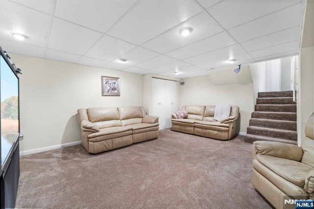 carpeted living room with a drop ceiling, stairway, and baseboards