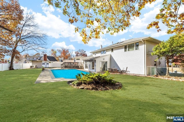 rear view of house with a fenced backyard, a fenced in pool, and a lawn