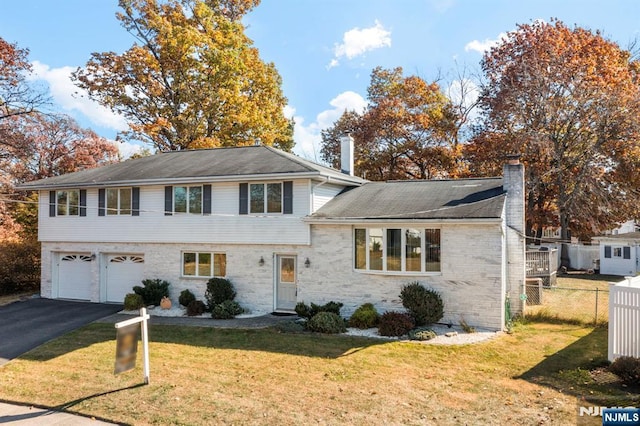 split level home featuring aphalt driveway, a chimney, a front yard, fence, and a garage