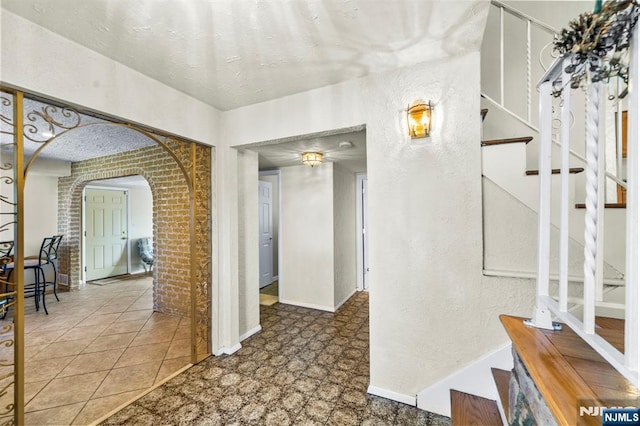 corridor featuring arched walkways, brick wall, stairs, and baseboards