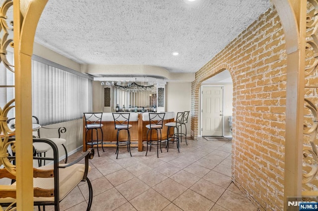 interior space with arched walkways, a textured ceiling, brick wall, baseboards, and tile patterned floors