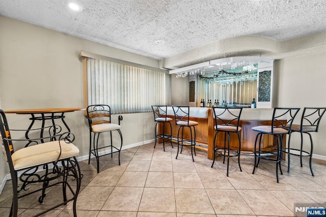 interior space featuring a textured ceiling, tile patterned flooring, bar area, and baseboards