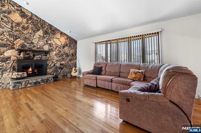 living area featuring lofted ceiling, wood finished floors, and a stone fireplace