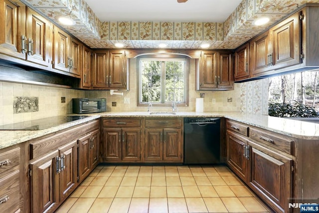 kitchen with light tile patterned floors, light stone countertops, a sink, black appliances, and backsplash