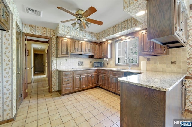 kitchen featuring visible vents, wallpapered walls, a peninsula, a sink, and decorative backsplash