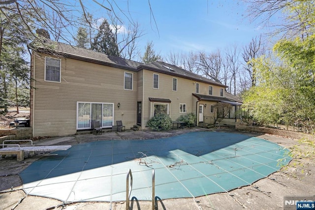 back of house with a covered pool, a patio area, and a chimney