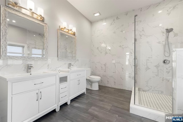 bathroom featuring tile walls, a marble finish shower, double vanity, toilet, and a sink