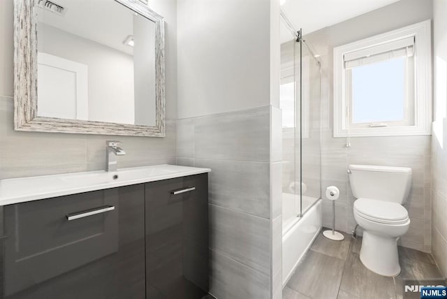 full bath featuring toilet, vanity, visible vents, and tile walls