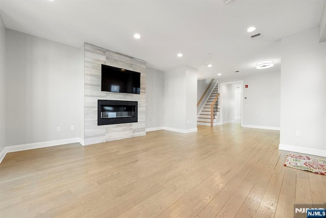 unfurnished living room featuring a tile fireplace, visible vents, baseboards, light wood-style floors, and stairway