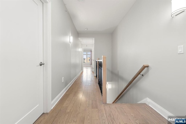 hallway with baseboards, light wood finished floors, an upstairs landing, and attic access