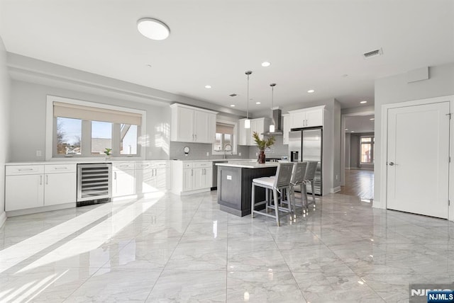 kitchen with visible vents, wall chimney exhaust hood, wine cooler, marble finish floor, and stainless steel appliances