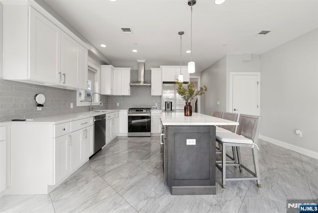 kitchen featuring visible vents, a center island, stainless steel appliances, wall chimney range hood, and a sink