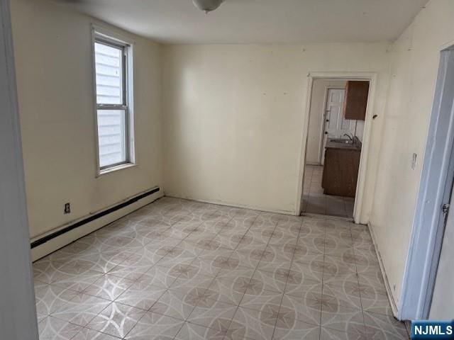 spare room featuring a baseboard heating unit and a sink