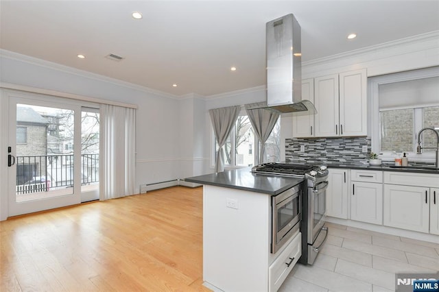 kitchen with island exhaust hood, a sink, dark countertops, white cabinetry, and stainless steel gas range oven