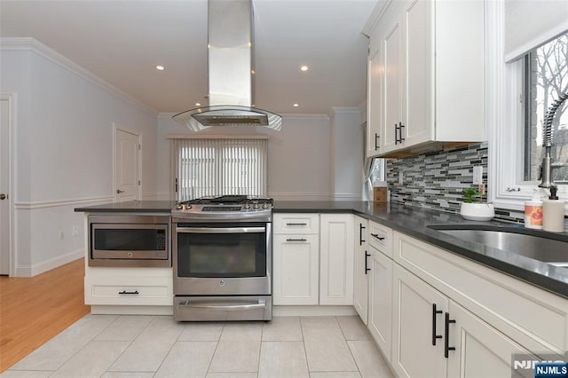 kitchen featuring dark countertops, a sink, island exhaust hood, stainless steel appliances, and ornamental molding