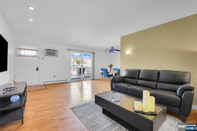 living area featuring light wood-type flooring, a baseboard radiator, a wall mounted air conditioner, and plenty of natural light