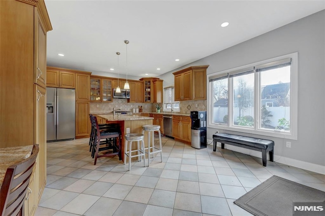 kitchen featuring stainless steel appliances, tasteful backsplash, a center island with sink, and brown cabinetry