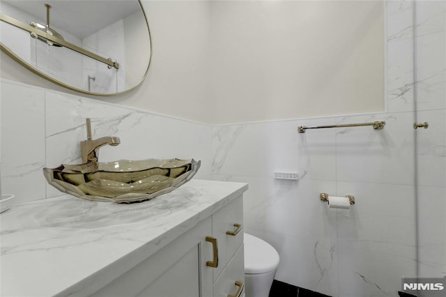 bathroom with vanity, tile walls, toilet, and a shower