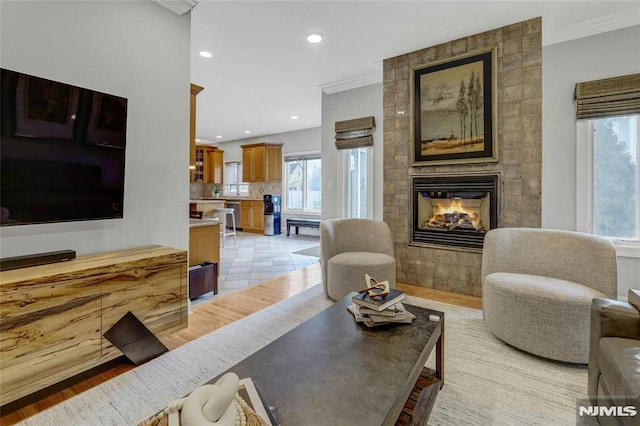 living room with recessed lighting, light wood finished floors, a tiled fireplace, and crown molding