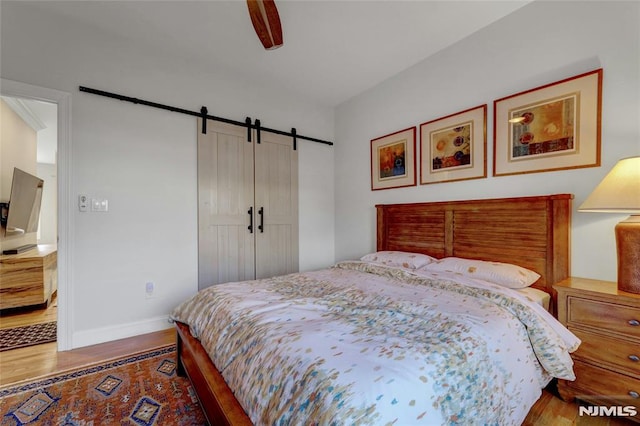 bedroom with ceiling fan, baseboards, a barn door, and wood finished floors