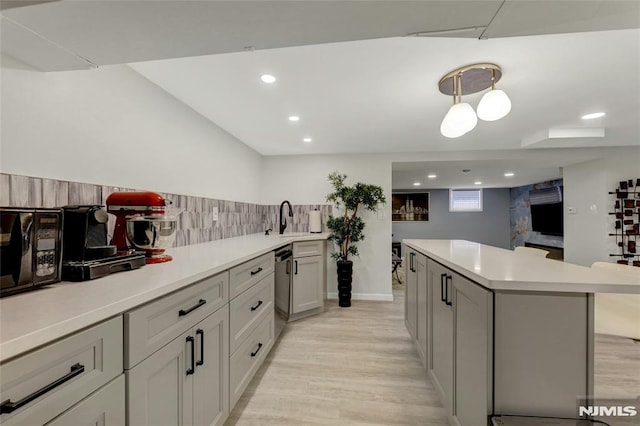 kitchen with a sink, stainless steel dishwasher, a center island, light wood-style floors, and light countertops