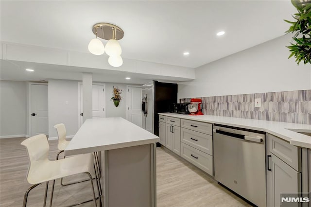 kitchen featuring a kitchen bar, tasteful backsplash, stainless steel appliances, light wood-style floors, and light countertops