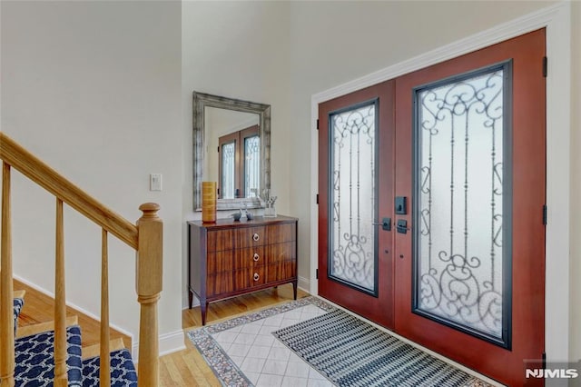 entrance foyer with light wood-type flooring, french doors, baseboards, and stairway