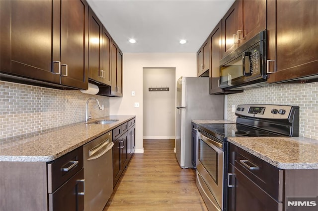 kitchen featuring light wood-style flooring, appliances with stainless steel finishes, a sink, dark brown cabinets, and baseboards