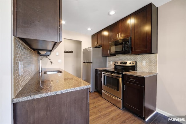 kitchen featuring stainless steel appliances, a sink, light wood-style floors, dark brown cabinets, and light stone countertops