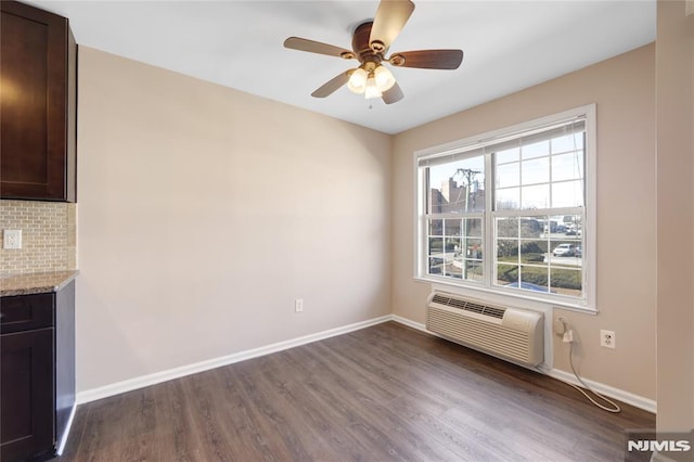 unfurnished dining area featuring a wall unit AC, baseboards, and dark wood finished floors