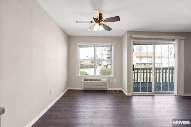 spare room featuring dark wood-style floors, a wall unit AC, baseboards, and a ceiling fan